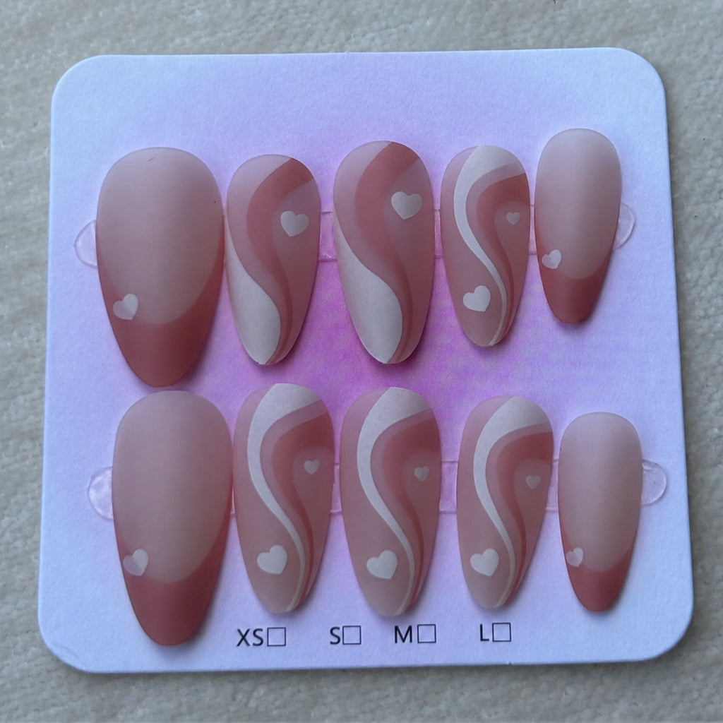 The full Swirl set of ten press-on nails on its card, matte dusty rose with white swirls and little hearts