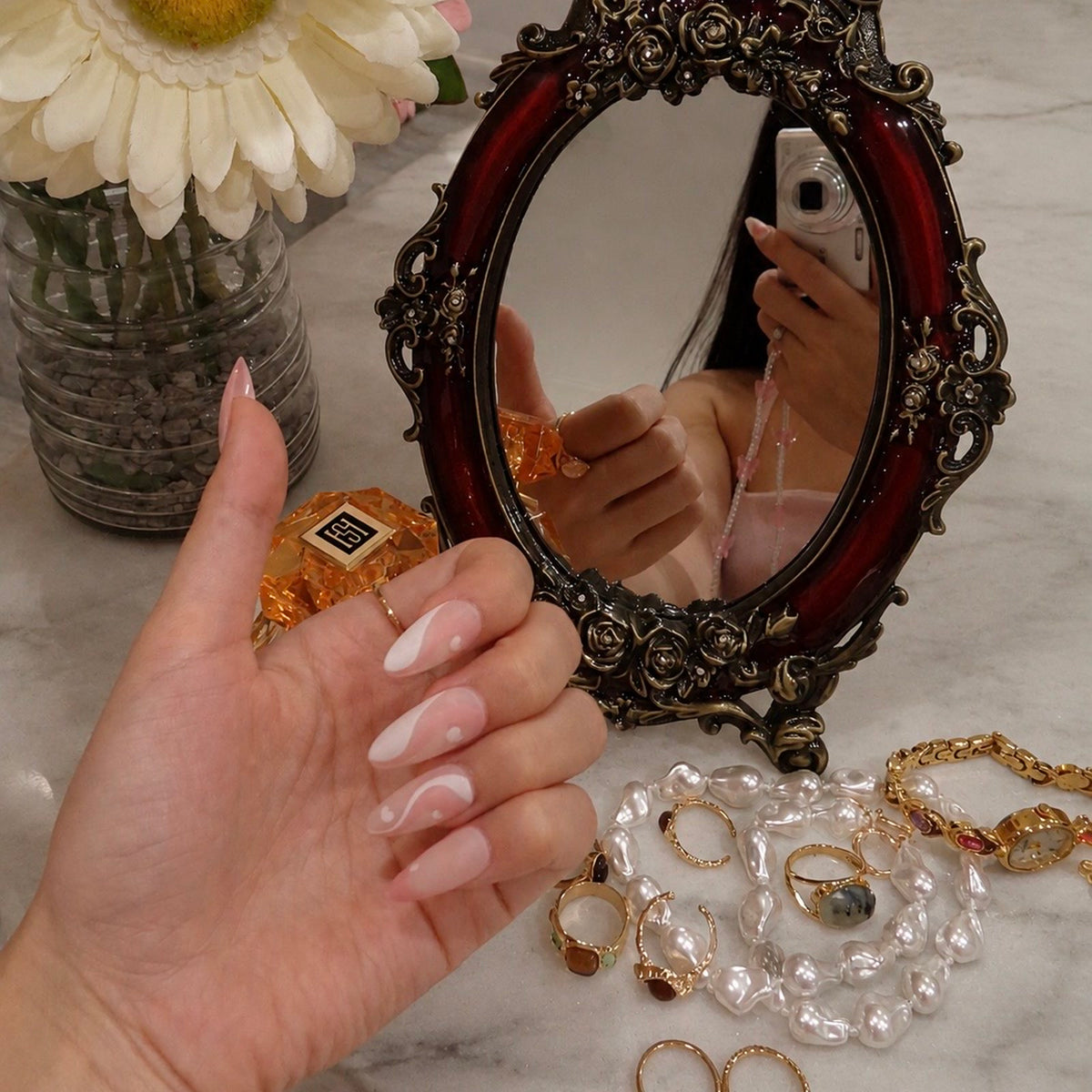 Swirl press-on nails, matte dusty rose with white swirls and little hearts, beside an antique mirror and pearls